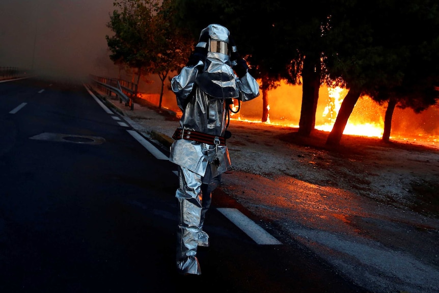 A firefighter wears a flame resistant uniform as wildfire burns in the town of Rafina.
