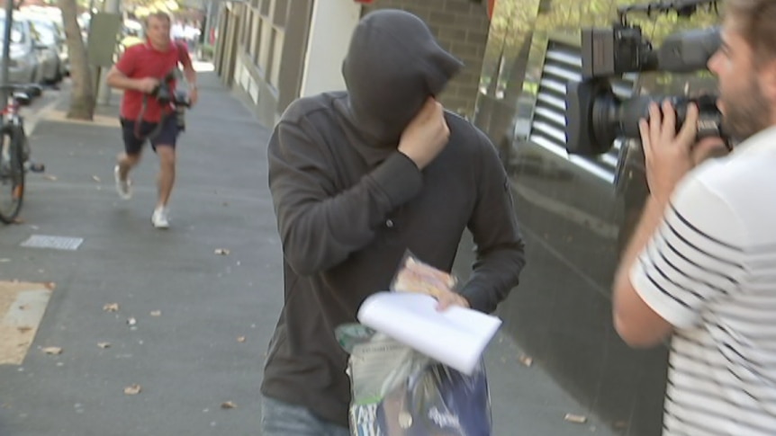A man covers his face with a hoodie to avoid the TV crews.