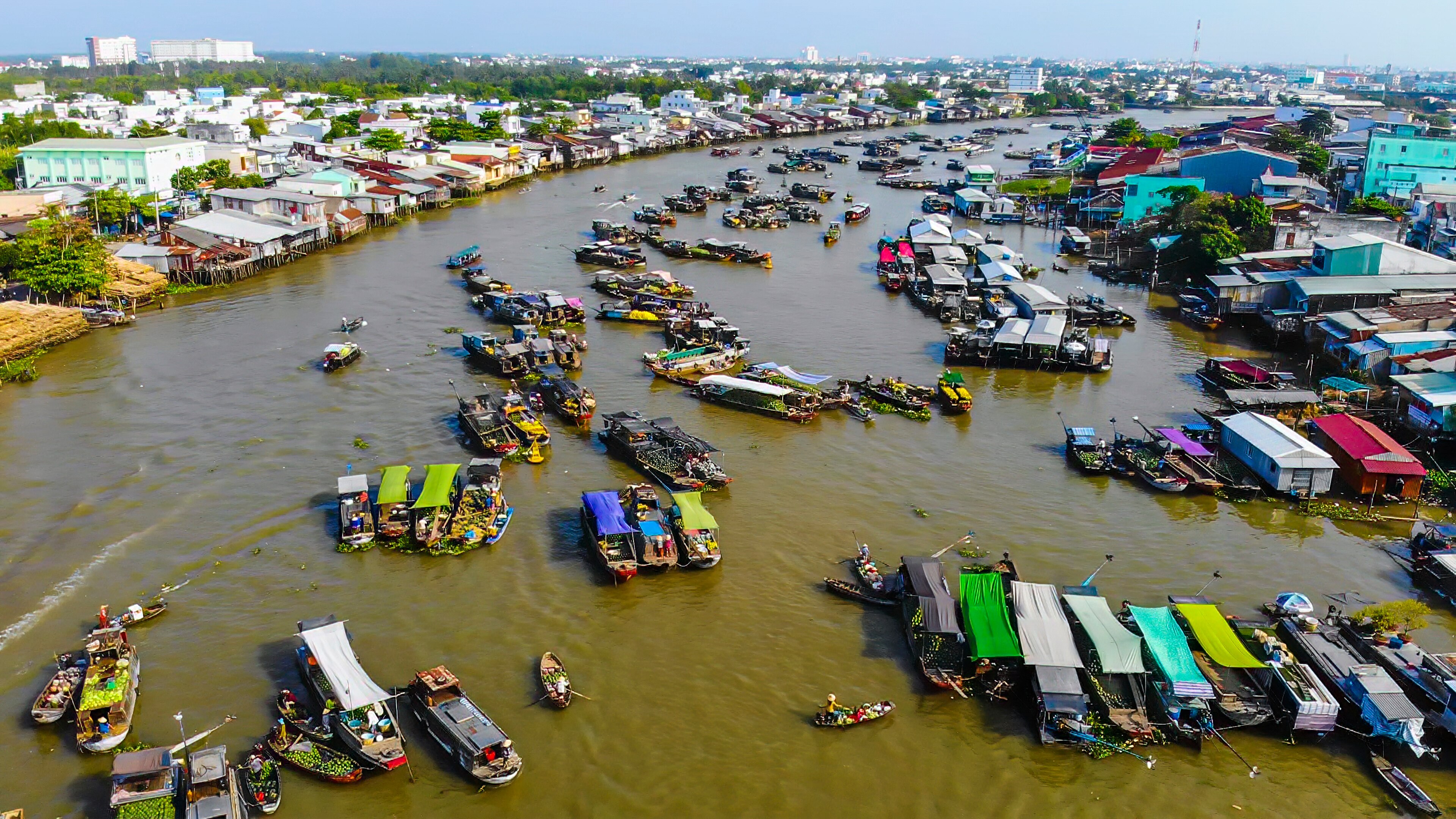 A vast river, crowded with small trading vessels and boarded by shacks and shops.
