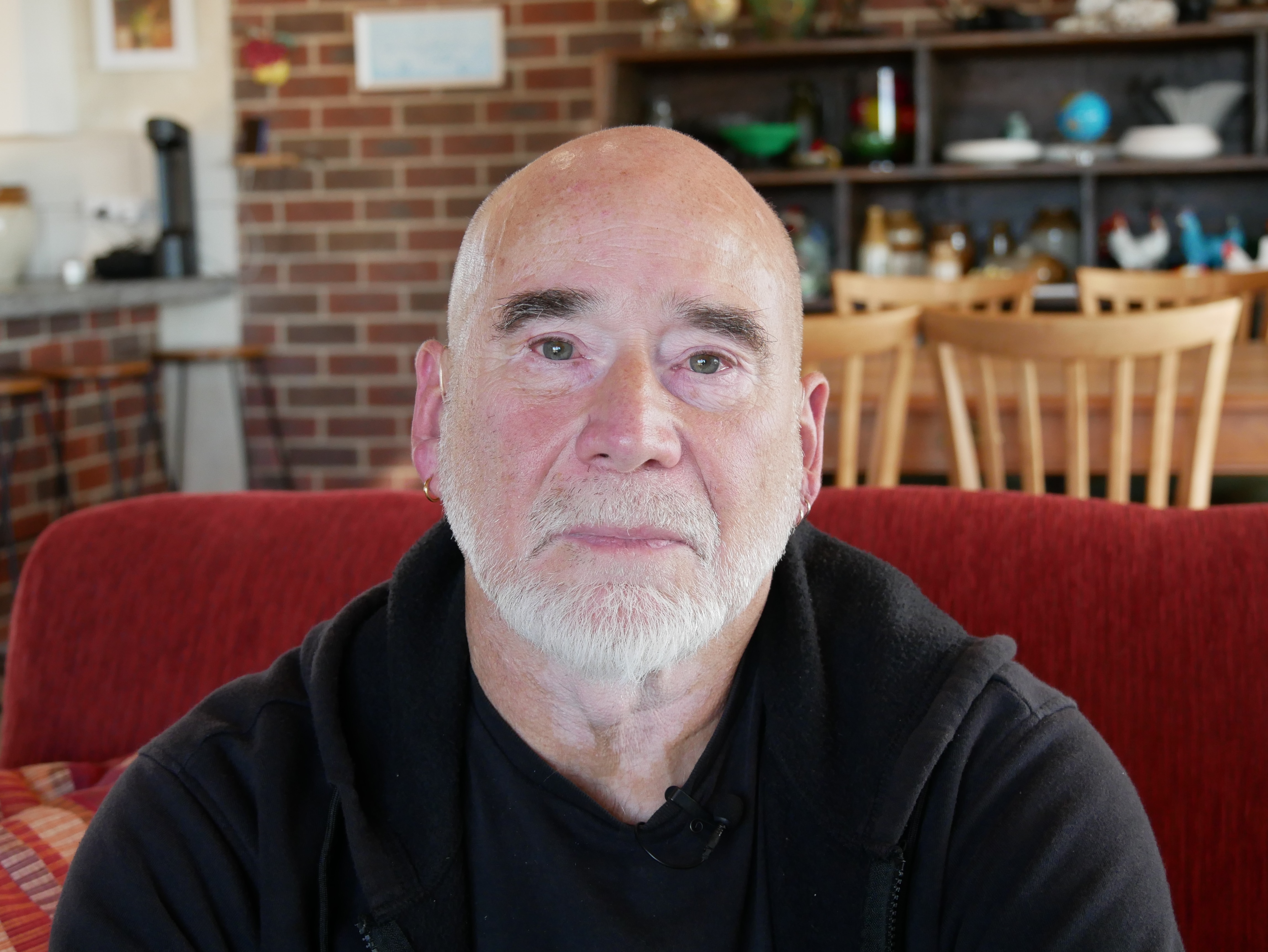 A man with a white beard sits on a red sofa