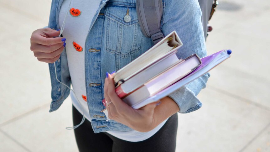 A university student with blue nail polish carries a pile of text books.