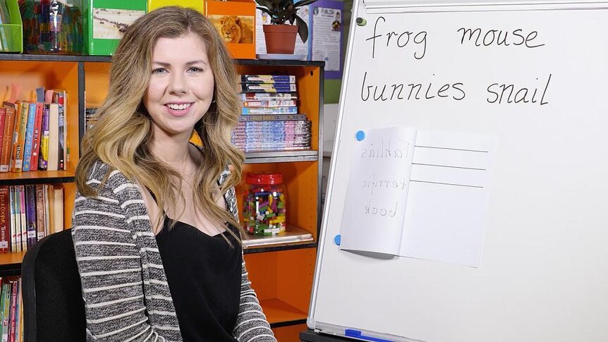 Female teacher sits in front of whiteboard with words frog mouse bunnies snail