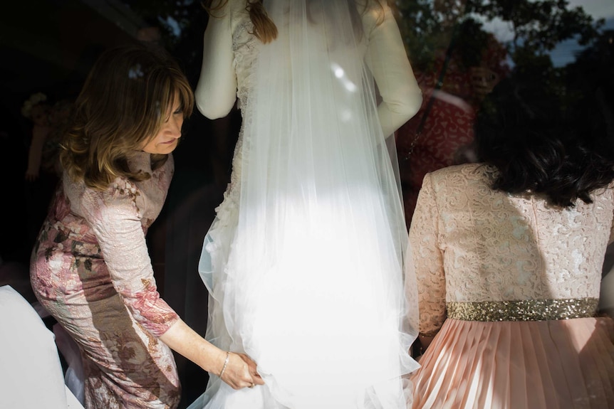 A women bends down to straighten the train on a bride's wedding dress.
