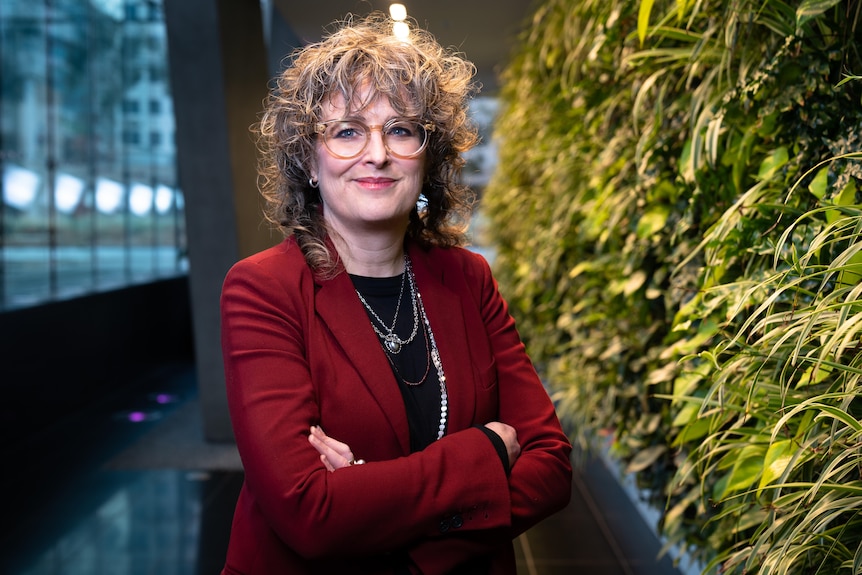 une femme sourit à la caméra dans le hall d'un immeuble de bureaux.