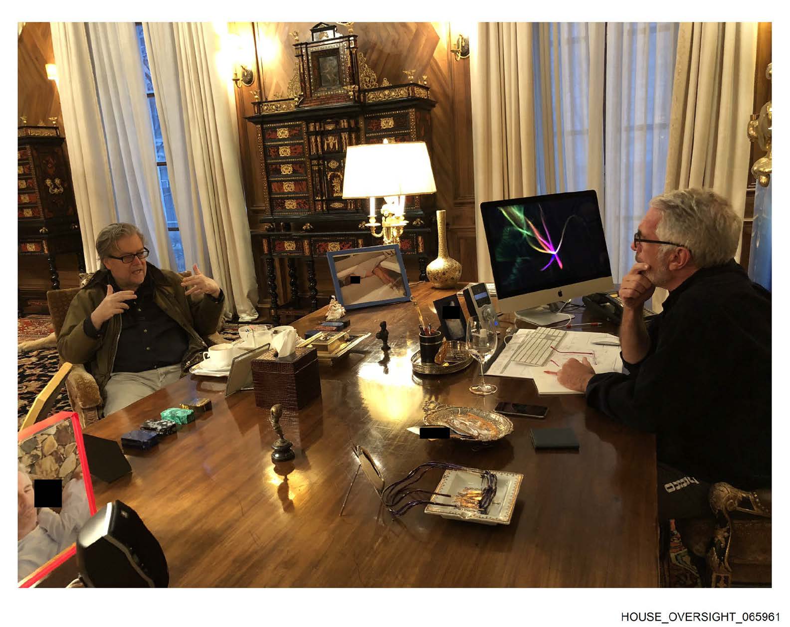 Steve Bannon está sentado ao lado de uma mesa e conversa com Jeffrey Epstein, que está sentado do outro lado.