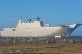 A large warship with a helicopter on its deck just off land in the ocean