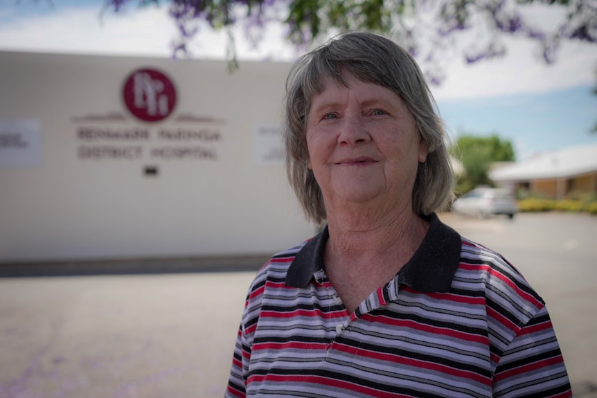 A woman with grey hair standing in front of a blurred hospital