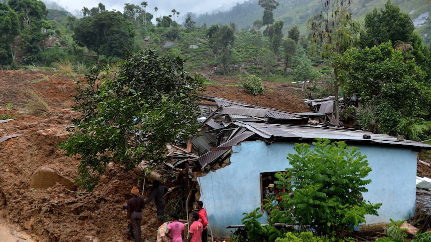 Sri Lankan residents stand outside a damaged building at the site of a landslide caused by heavy monsoon rains in Koslanda village in central Sri Lanka on October 29, 2014.