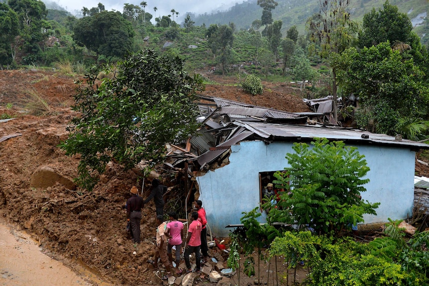 Sri Lankan residents stand outside a damaged building at the site of a landslide caused by heavy monsoon rains in Koslanda village in central Sri Lanka on October 29, 2014.