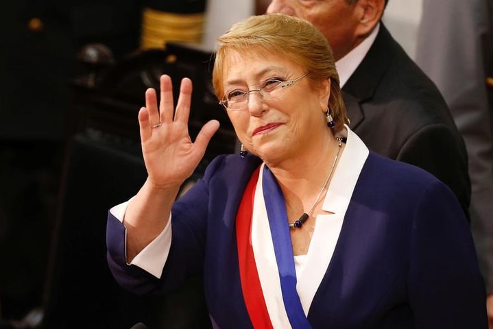 Michelle Bachelet waves and smiles wearing a red, white and blue sash, the colours of Chilean flag.