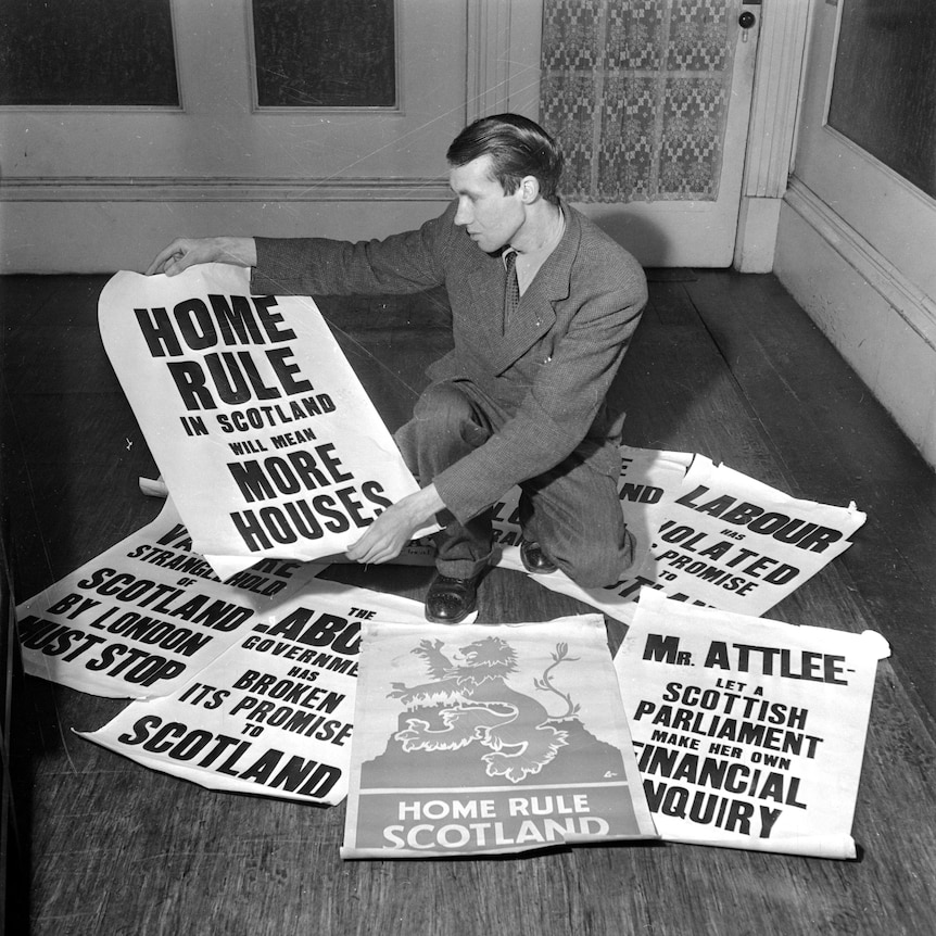 A man sits, surrounded by posters calling for Home Rule for Scotland.