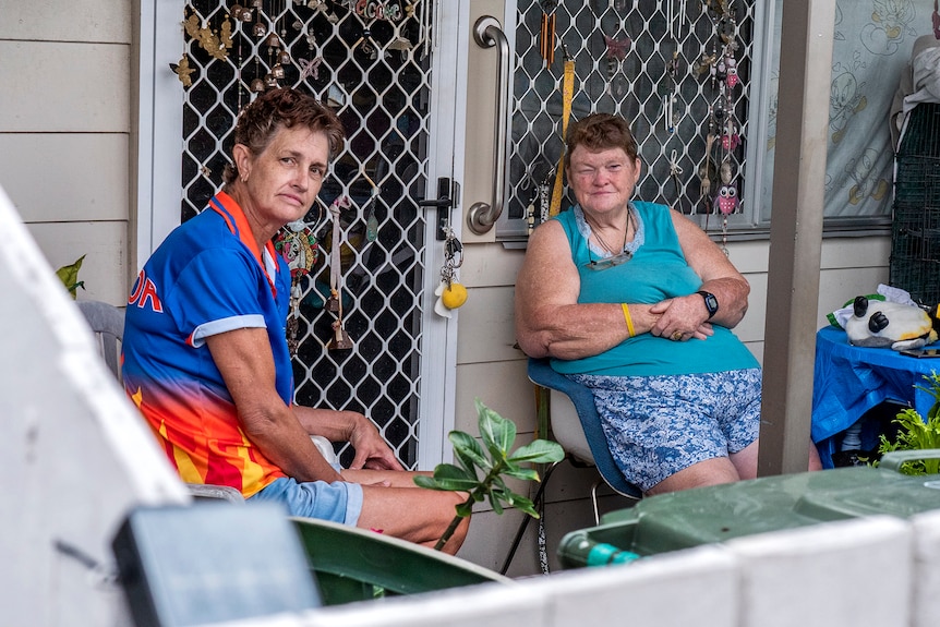 Two women sit outside a house like they are talking.