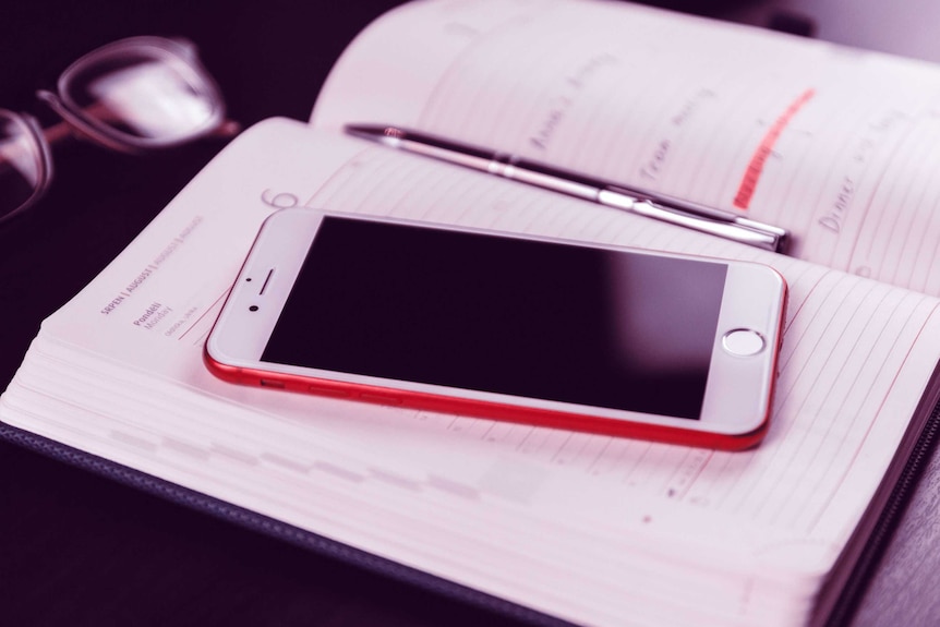 A red smartphone sits on top of an open diary page.