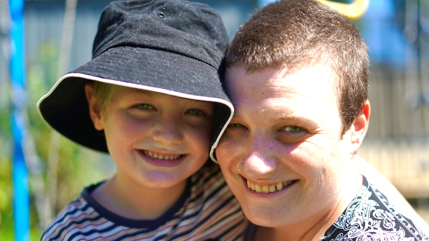 A woman wearing a hat hugs a little boy and both are smiling.