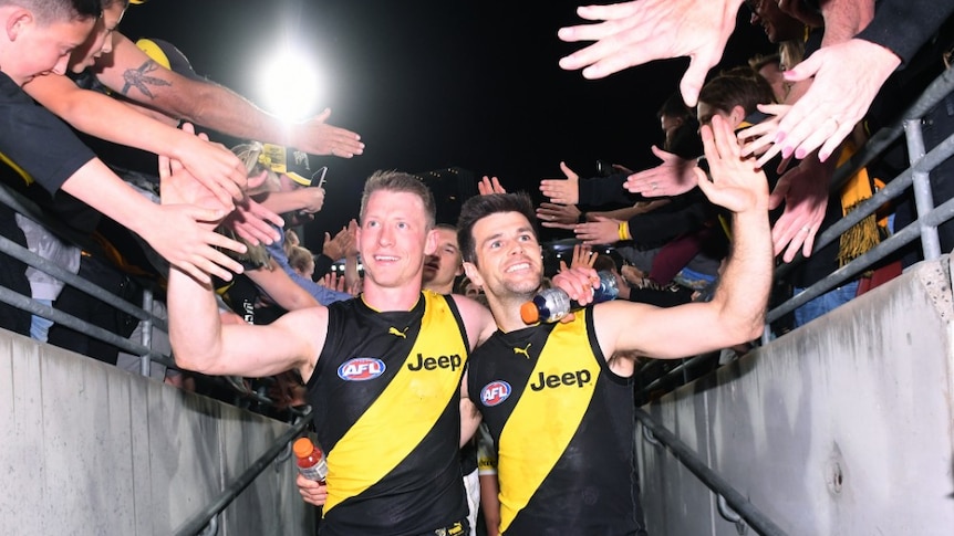 Richmond Tigers Trent Cotchin and Dylan Grimes walk off the field high-fiving people in the stands.