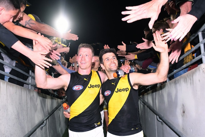 Richmond Tigers Trent Cotchin and Dylan Grimes walk off the field high-fiving people in the stands.