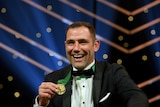 Cameron Smith holds up his gold Daly m medal while smiling.