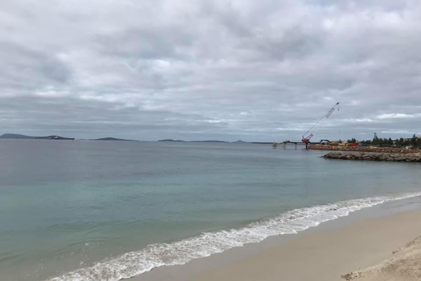 A crane removes the last of the jetty on a cloudy day.