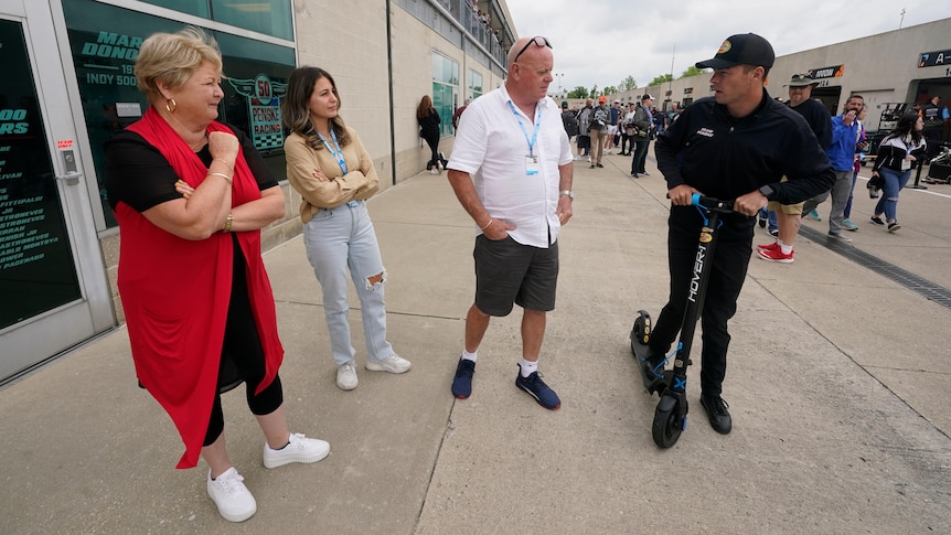 IndyCar driver Scott McLaughlin props on a scooter as he talks to three members of his family at a speedway.