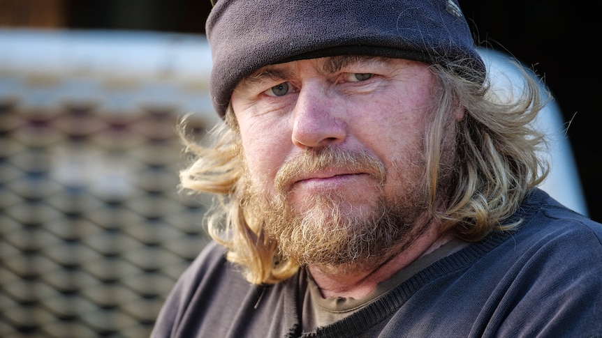 A portrait of a man with blond hair and a beard, wearing a navy pullover and beanie.