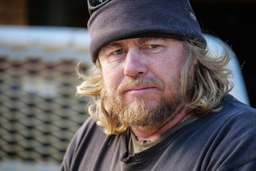 A portrait of a man with blond hair and a beard, wearing a navy pullover and beanie.