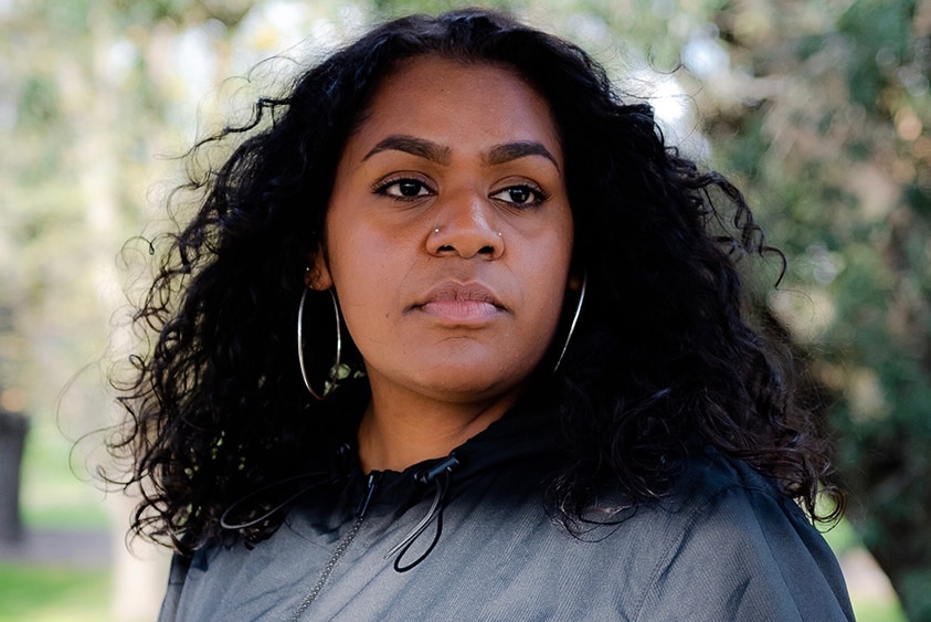 Miiesha is wearing big silver hoops and a black hoodie. She is looking off-camera with a serious face.