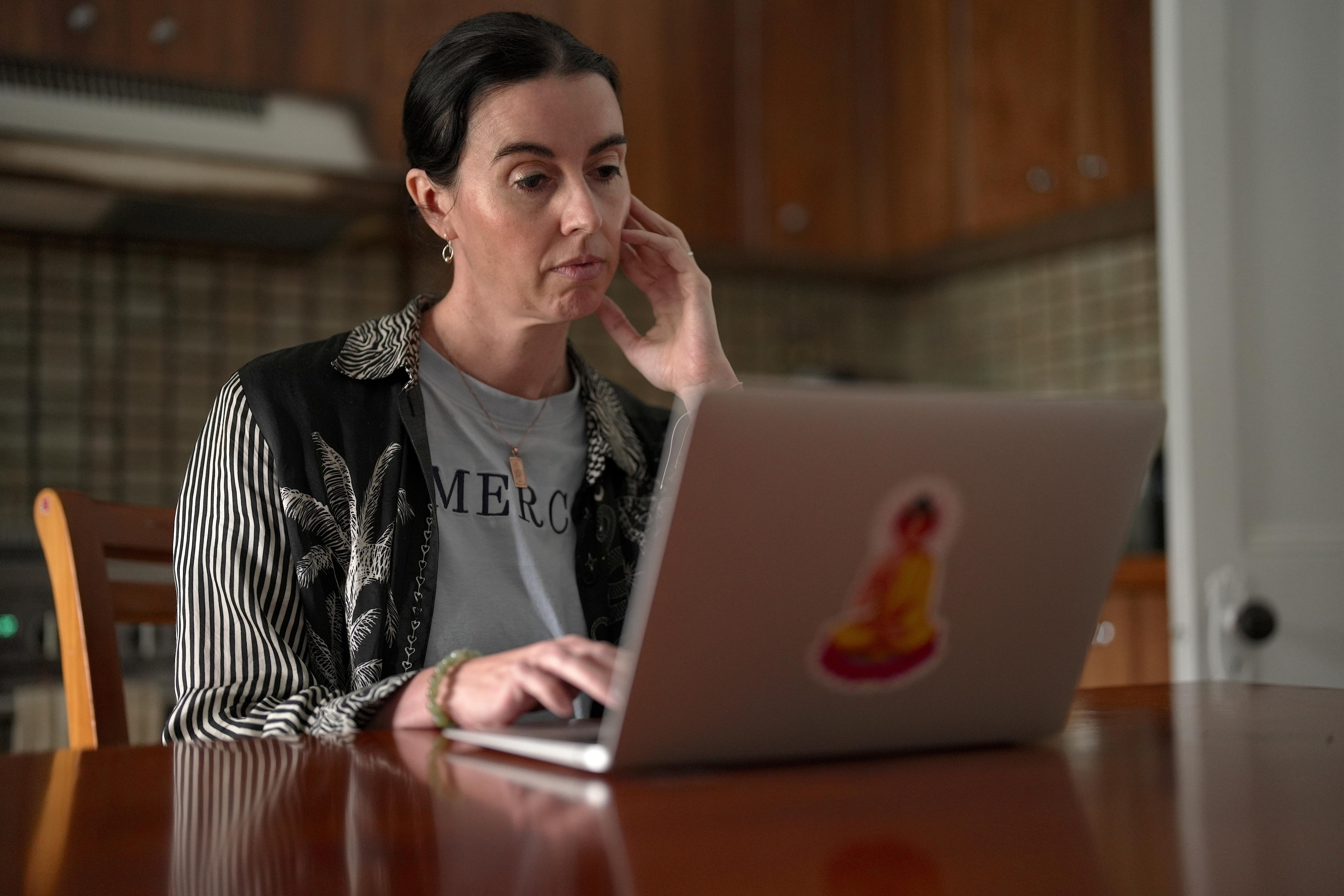 A woman sits at a table with a laptop open.