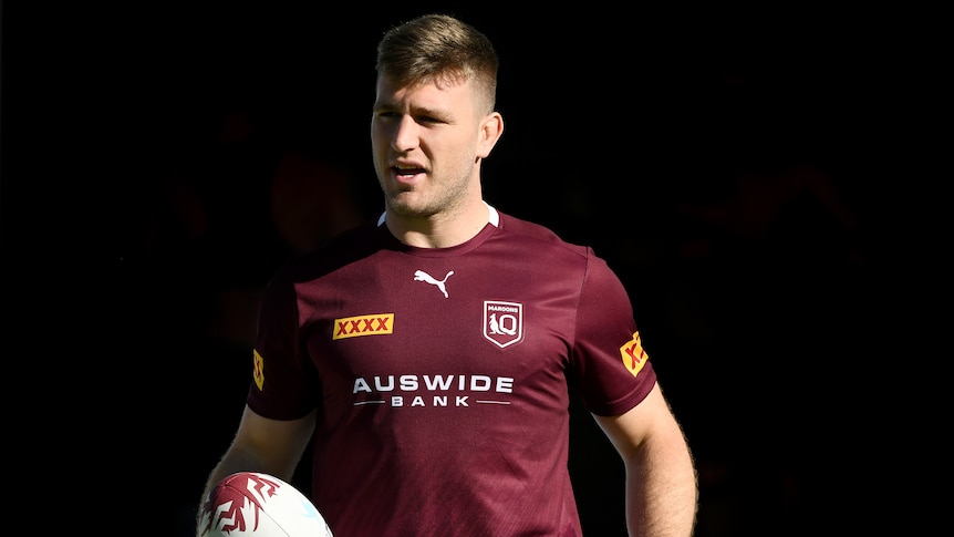 A Queensland Maroons State of Origin player holds a football in his right hand at a training session.