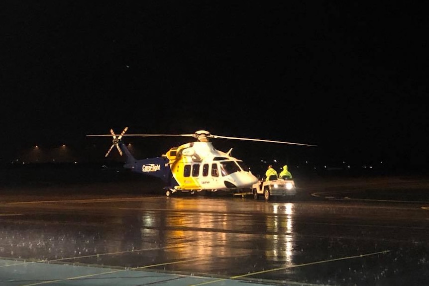A helicopter on the tarmac at night time with the rain coming down.