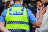 A police officer wearing a high-vis vest with the word 'Police' on the back speaking to two people.