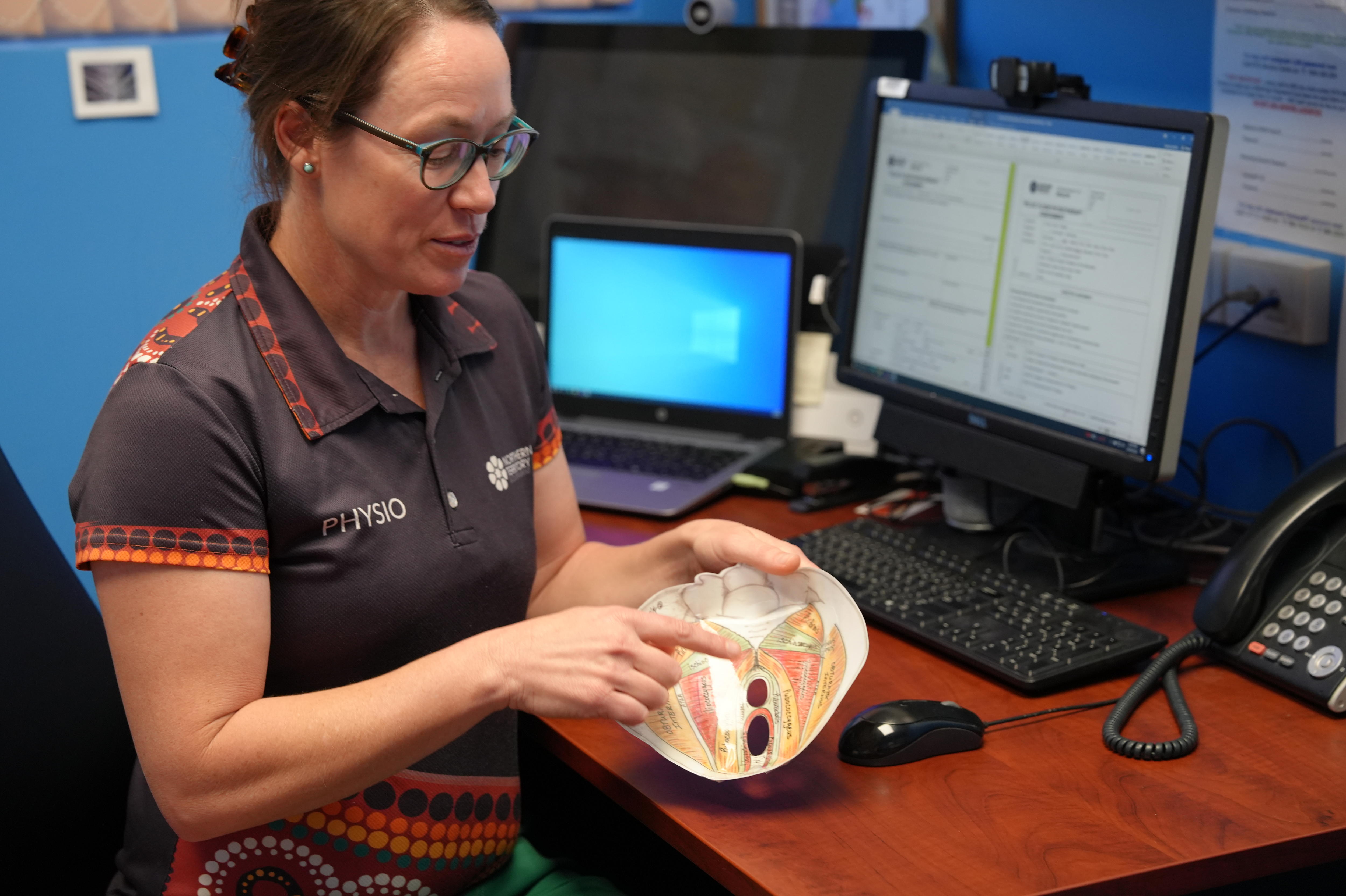 A women sitting in a chair pointing to a model pelvic floor