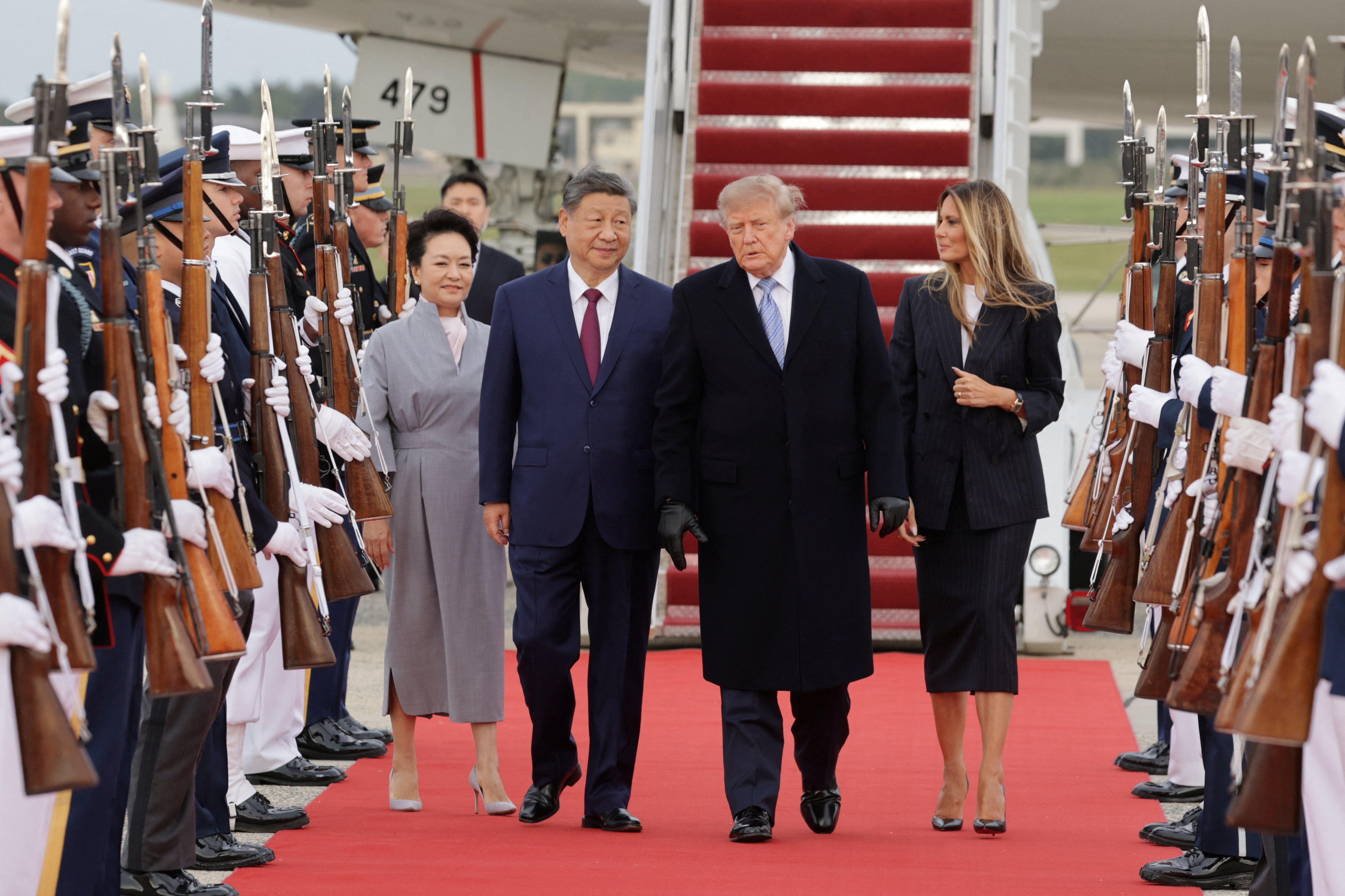 Two couples walk down a red carpet with ceremonial troops holding guns on either side