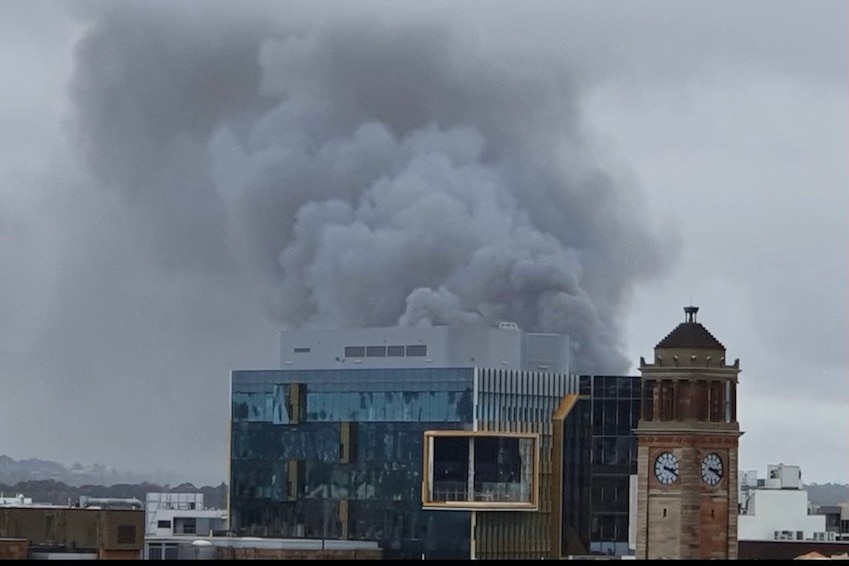 Thick smoke from a fire is seen behind a cityscape.