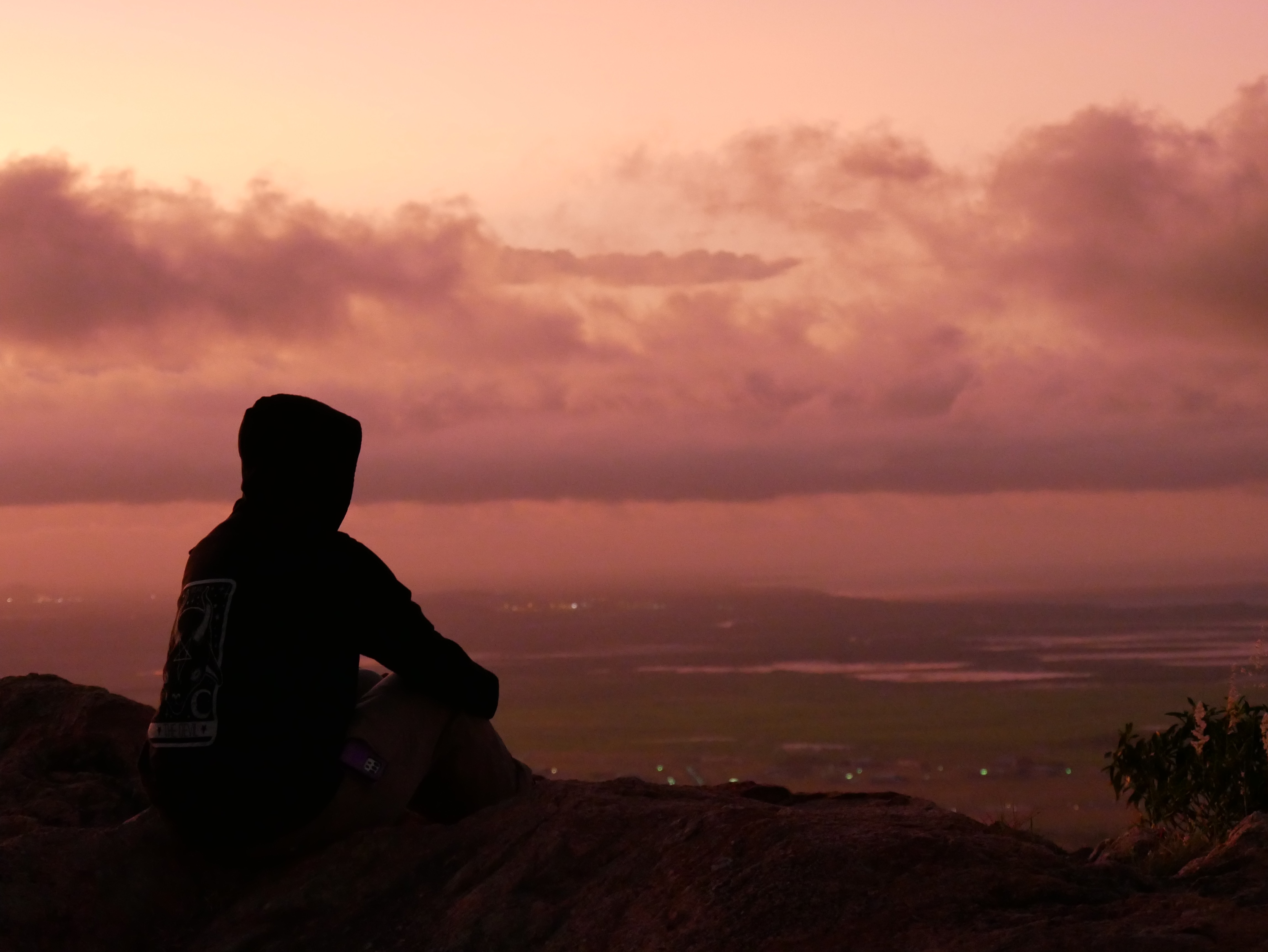 A silhouette of a person in a hoodie over wetlands at sunset.