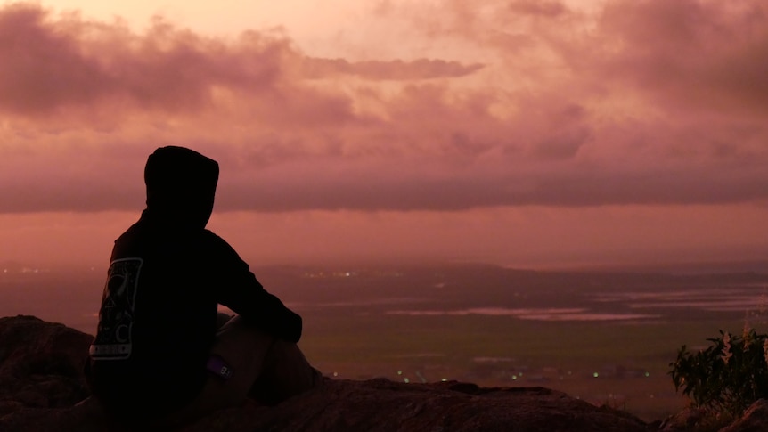 A silhouette of a person in a hoodie over wetlands at sunset.