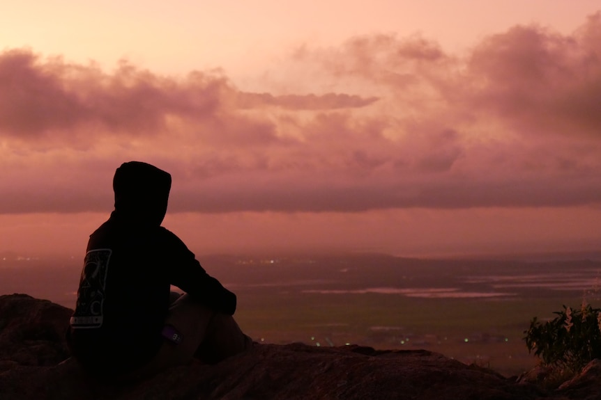 A silhouette of a person in a hoodie over wetlands at sunset.