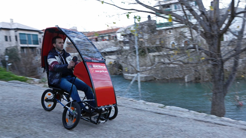A man rolls downhill in a small red folding car.