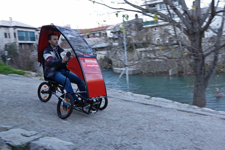 A man rolls downhill in a small red folding car.