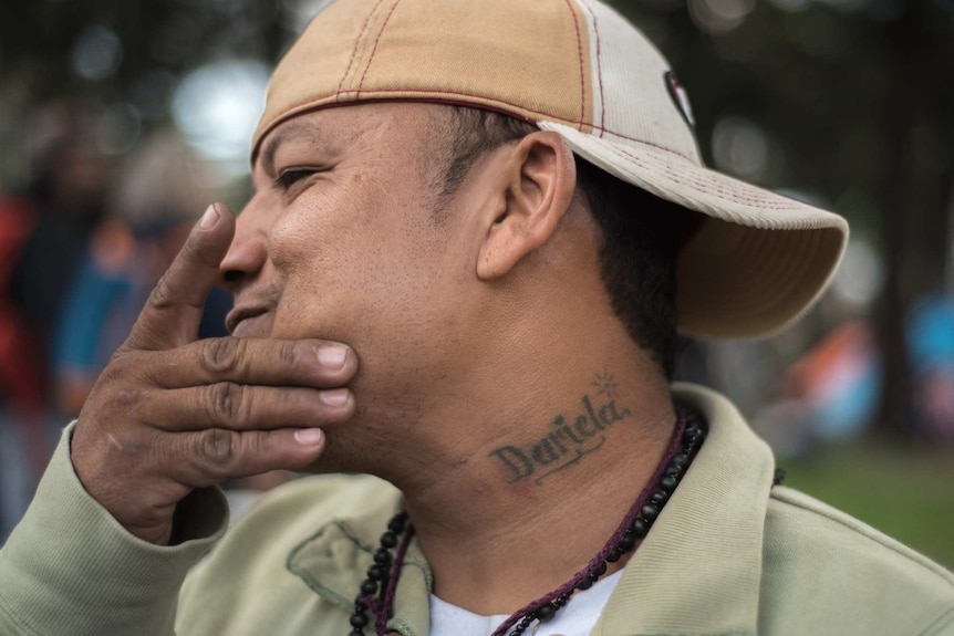 Francis Acosta in a cap shows off a tattoo on his neck that reads, Dariela