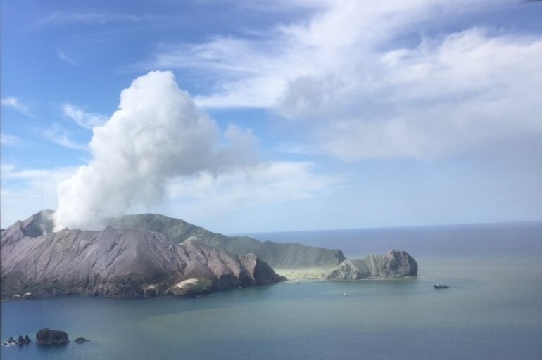 A massive plume of smoke rises after a deadly volcano eruption, photographed from a helicopter approaching an island.