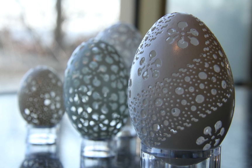 Three intricately carved eggshells sitting on small mounts on a bench