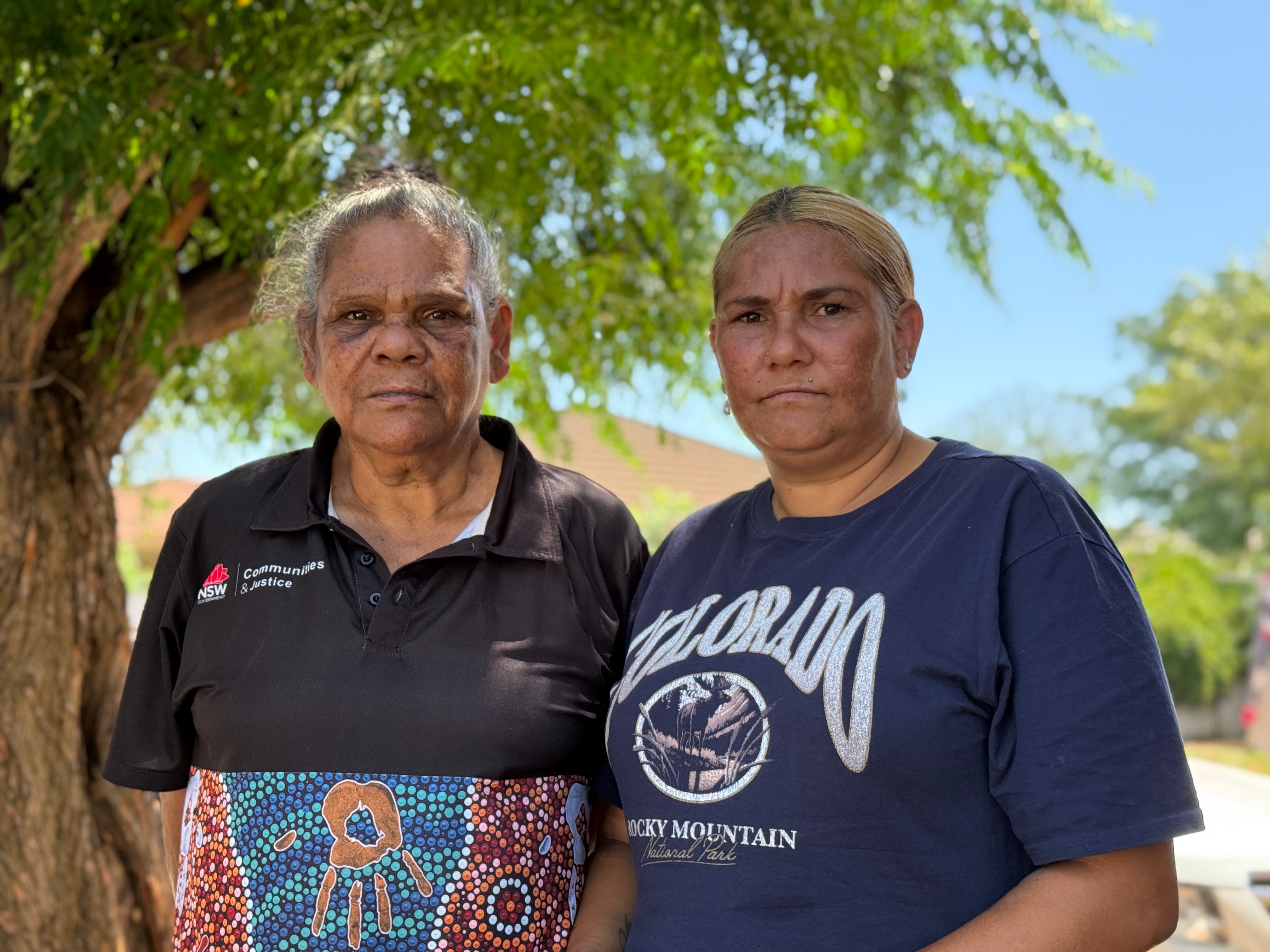 Two Indigenous women with grim expressions face the camera.