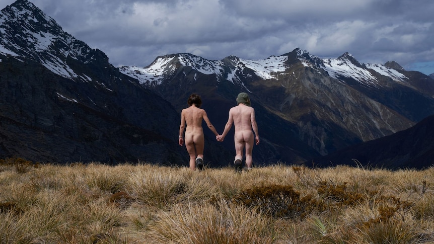 Two naked people seen from the back running towards mountains. 