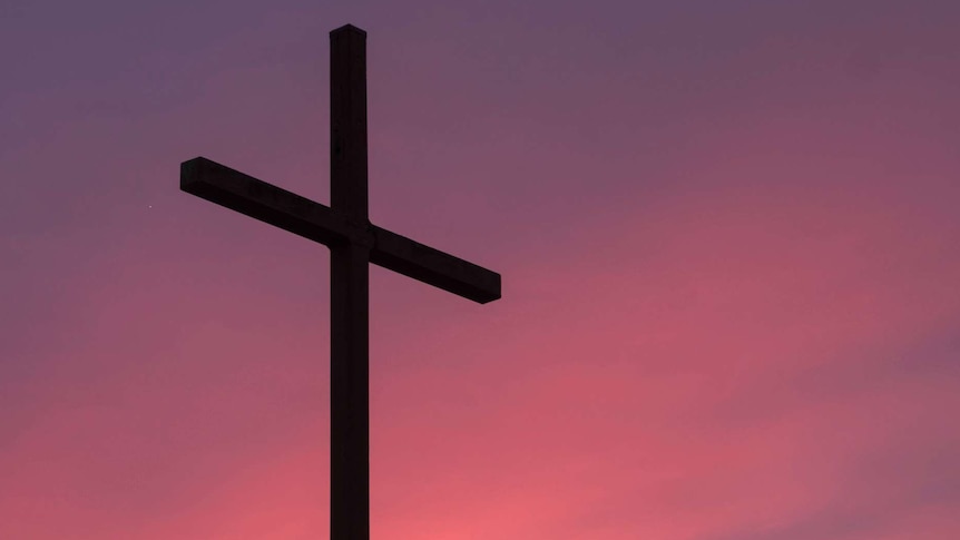 A large church cross with magenta sky behind.
