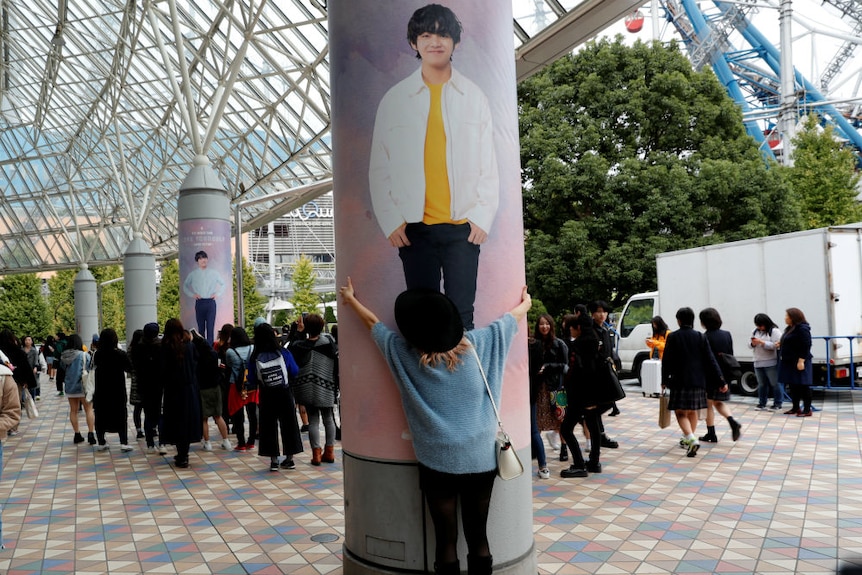 A woman hugs a large poll emblazoned with a poster of a member of BTS