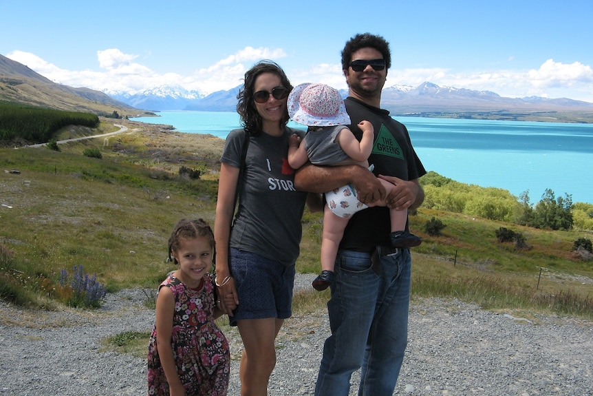 A smiling couple pictured with their young children at a scenic New Zealand landscape.