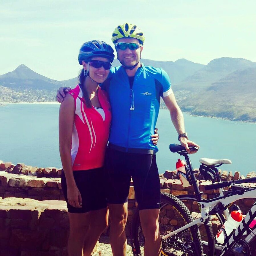 A man and a woman smile for the camera, posing with bicycles with helmets on their heads.