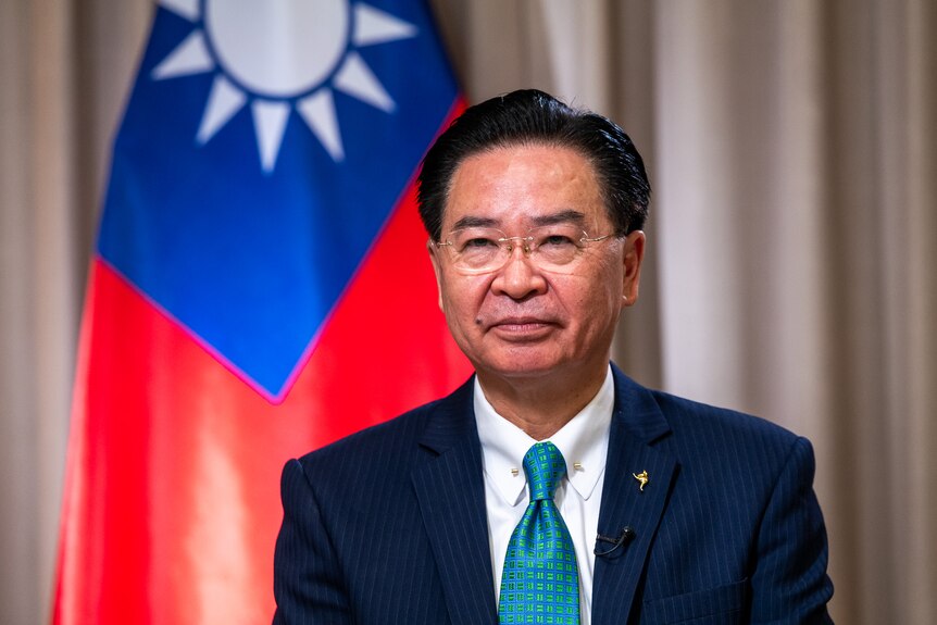 Joseph Wu, Taiwan Foreign Minister, wearing a navy suit and blue tie with the Taiwan flag behind him.