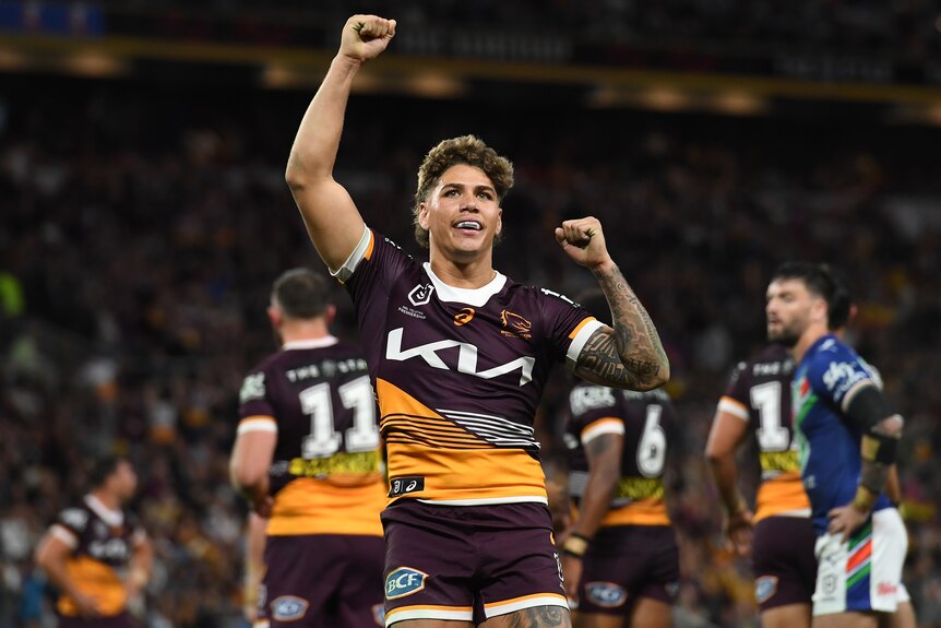 An NRL player with his fists raised in the air in triumph, smiling to a packed grandstand