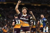 An NRL player with his fists raised in the air in triumph, smiling to a packed grandstand